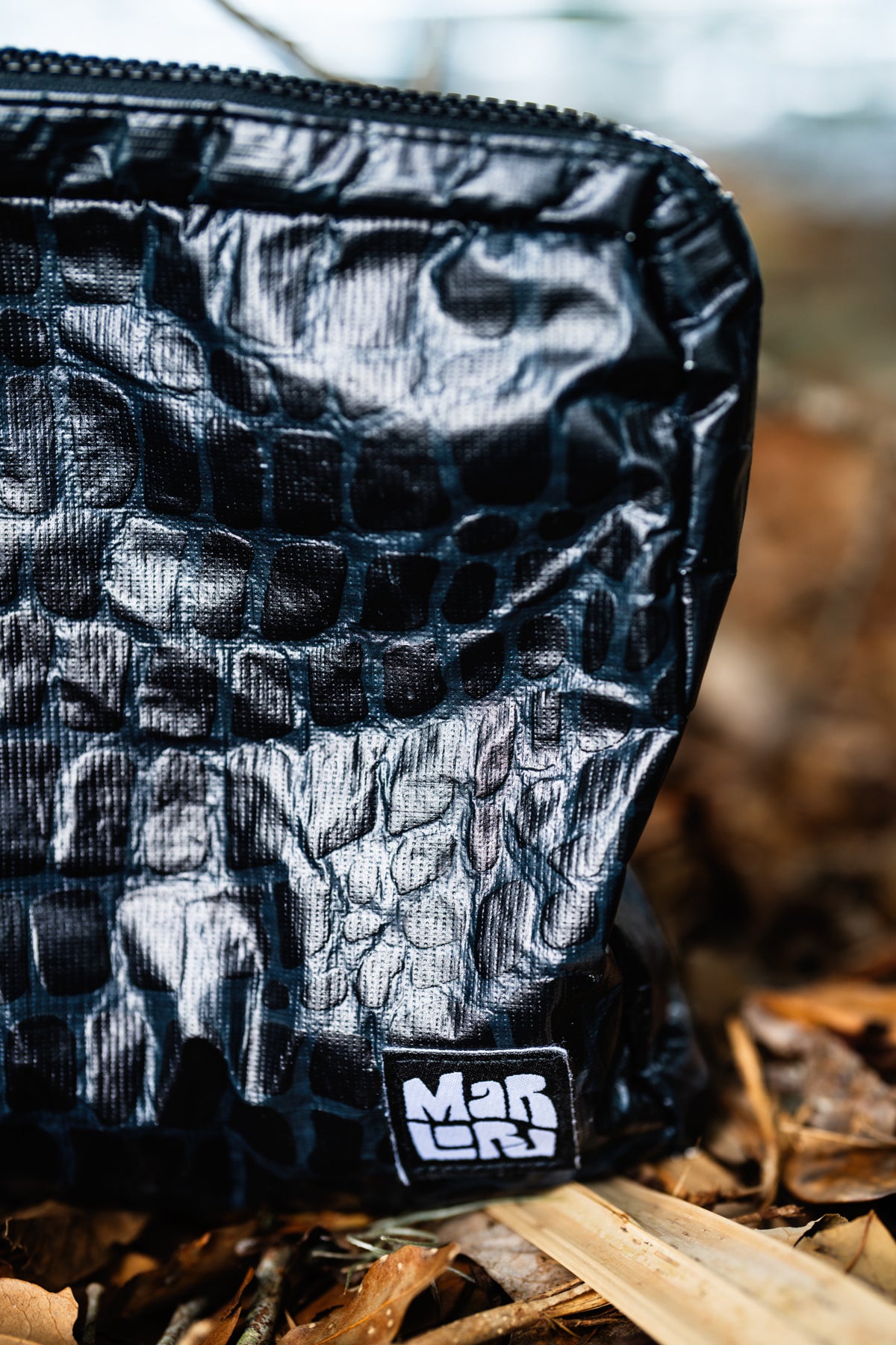 Close-up of the Gator Mid Pouch's glossy gator texture and Marloru patch, outdoors on fallen leaves